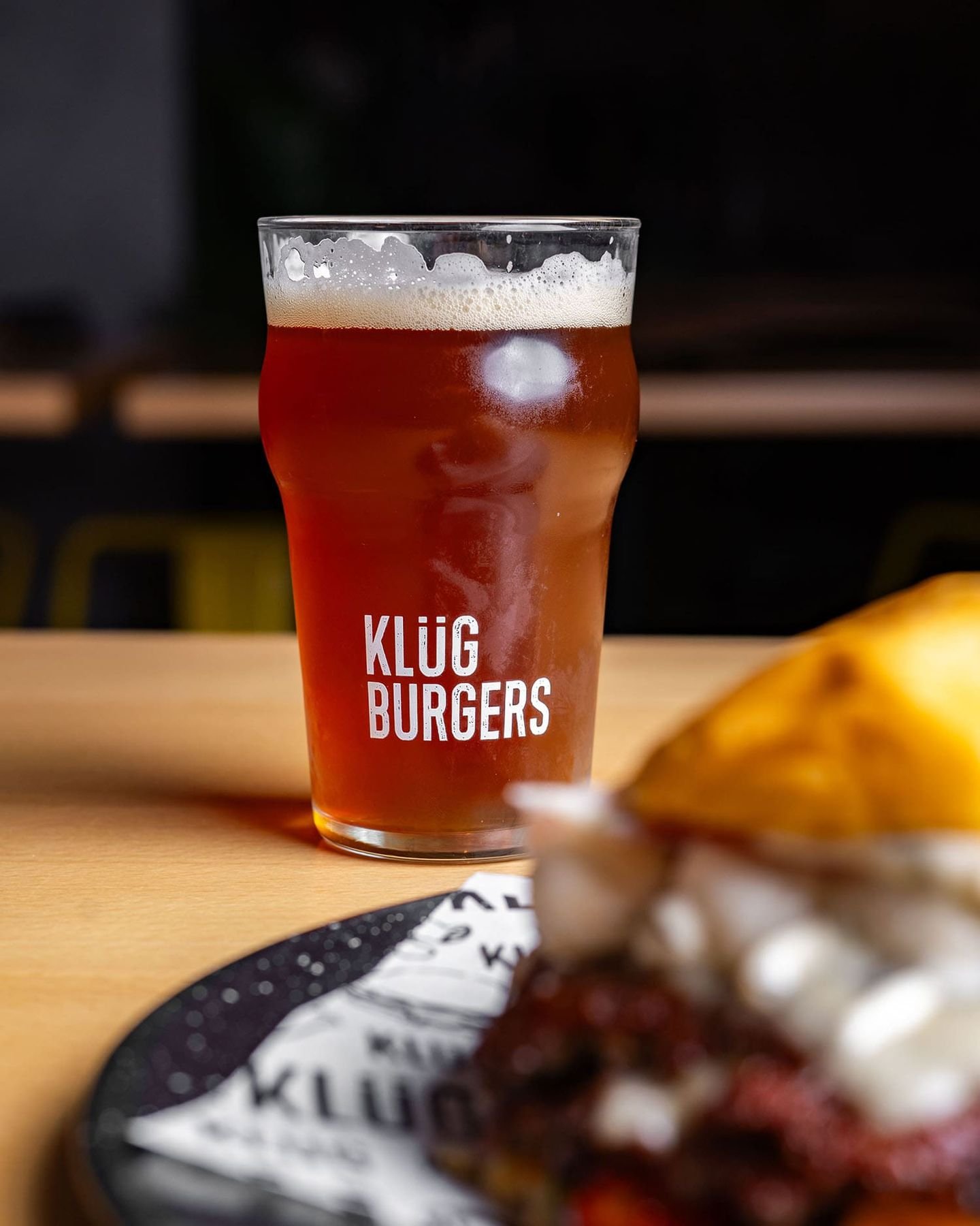 Pinta de cerveza con el logotipo de Klüg junto a una hamburguesa
