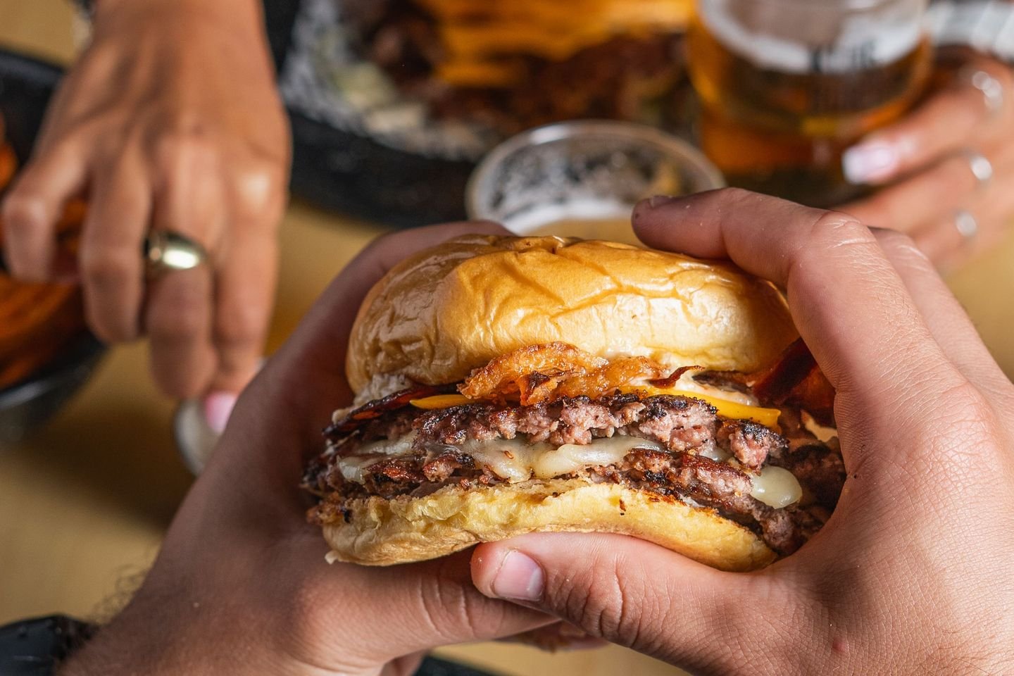 Dos personas sujetando hamburguesas sobre la mesa del local