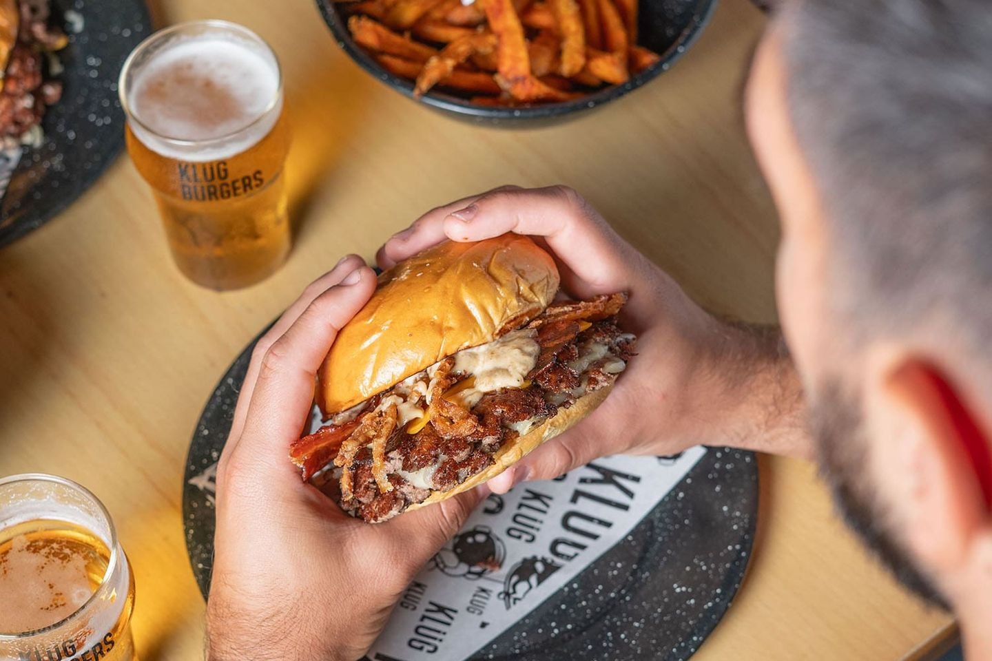 Cliente mordiendo una hamburguesa junto a una ración de boniatos