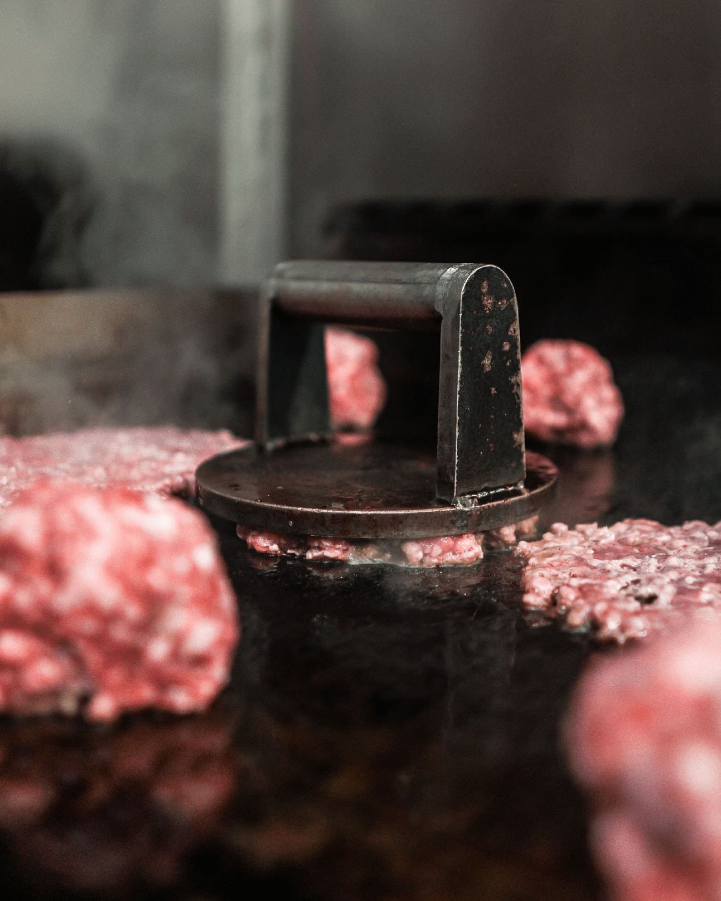 Prensa de smash aplastando un medallón de ternera sobre la plancha caliente